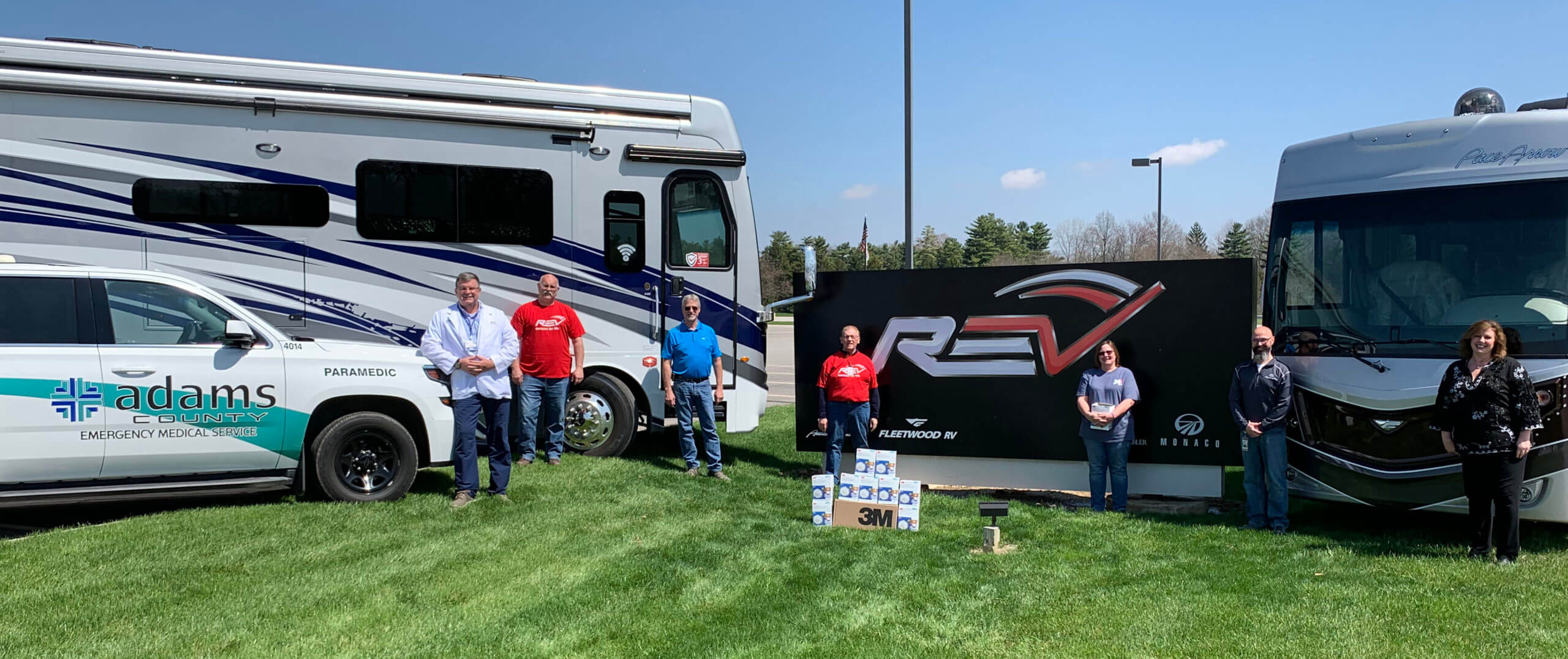 Image of REV RV's with people standing in front of them with a sign of REV Group logo