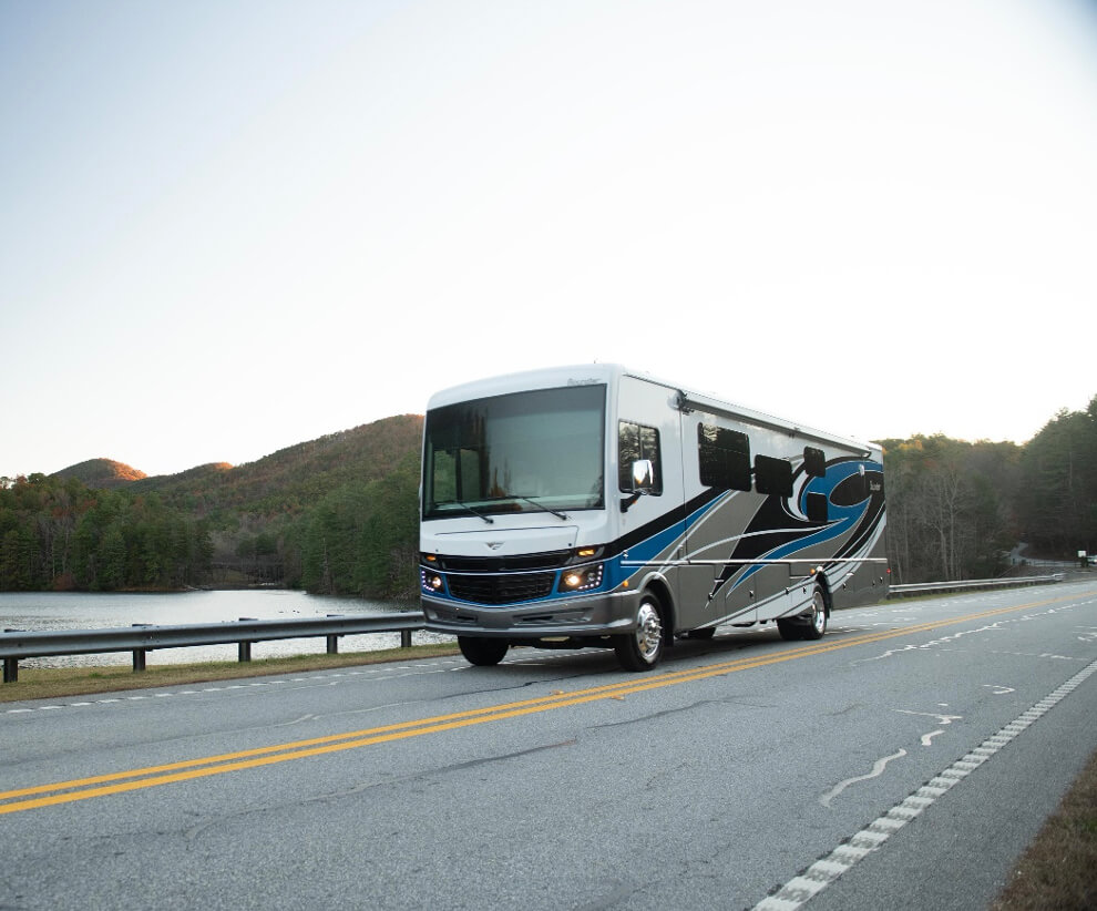 Fleetwood RV being driven down a road by a lake