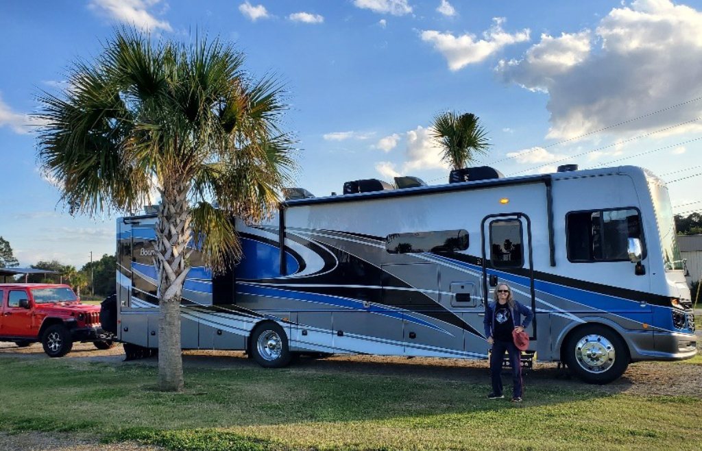 Image of a Fleetwood RV with a lady standing in front of it outside with palm trees