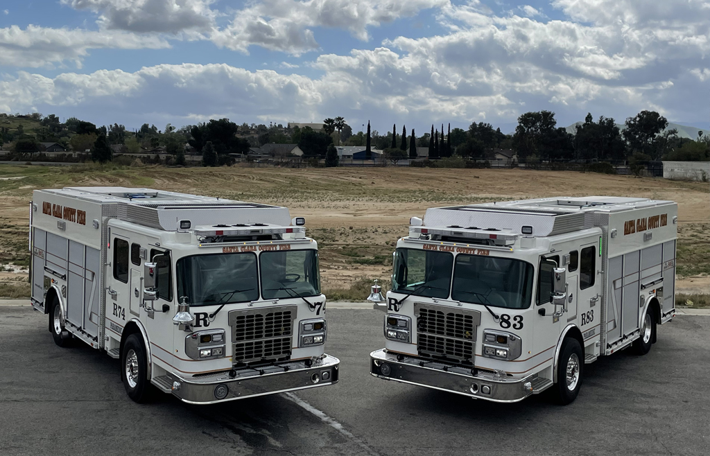 Image of two fully electric Vector Fire Trucks on a street with trees in the background