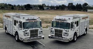 Image of two fully electric Vector Fire Trucks on a street with trees in the background