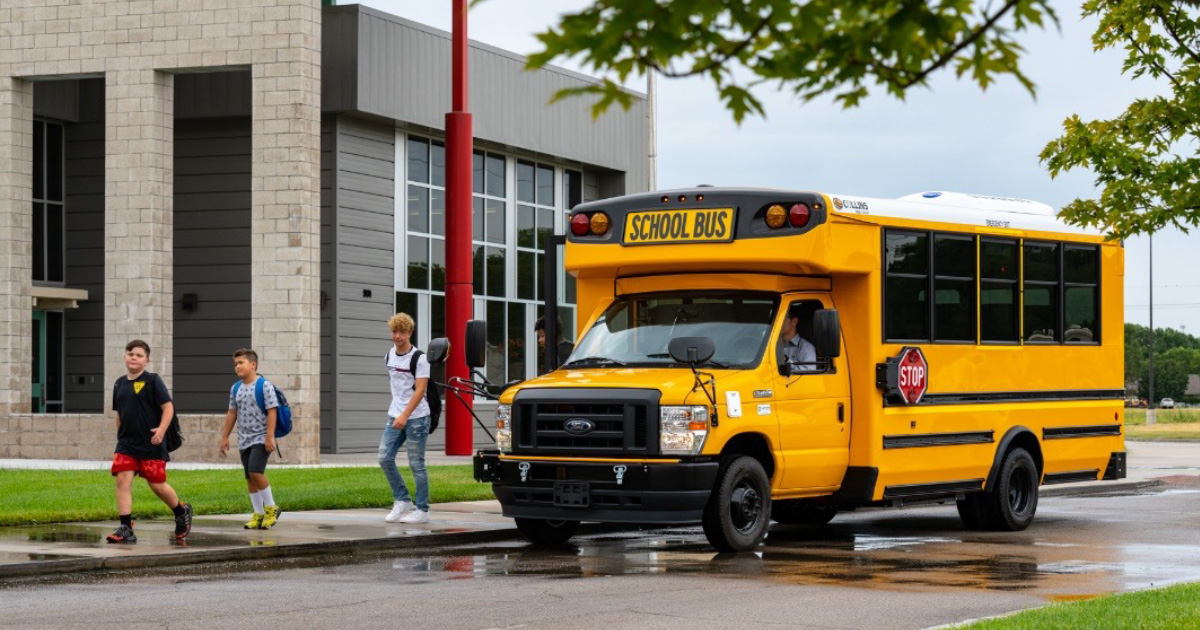 Collins electric school bus in front of a school with children getting off the bus.